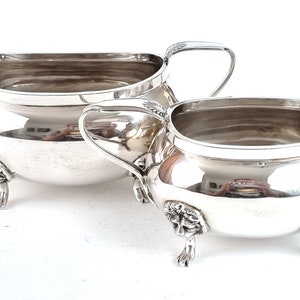 May include: A silver creamer and sugar bowl set with ornate feet and handles. The pieces are polished and have a shiny finish.