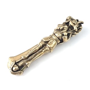 Peut inclure: Une figurine en métal couleur laiton représentant une créature hybride avec un groin de cochon, des oreilles de cerf et des sabots, vêtue d'une veste et d'une culotte. La base porte le texte en relief "TRUSTY SERVANT" sur une bannière.