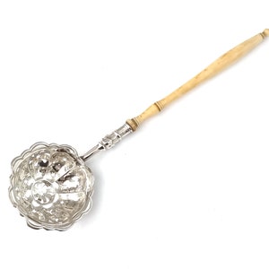 May include: A silver tea strainer with a decorative, pierced, round bowl and a long, ivory handle.