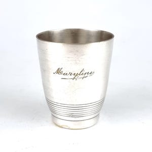 May include: Silver cup with a silver inscription that reads "Maryline" on the side. The cup has a silver band around the bottom.