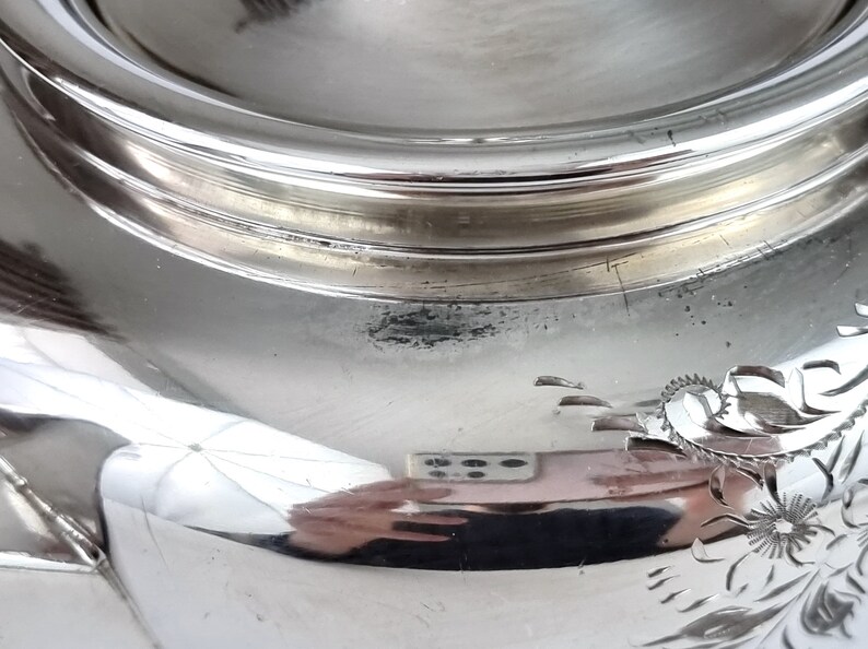 May include: Close-up of the bottom of a silver serving dish with a decorative floral design.