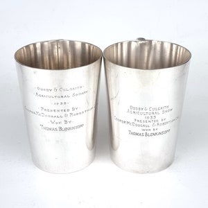 May include: Two silver cups with engraved text. The text reads "Ousby & Culgaith Agricultural Society 1935. Presented by Cooper McDougall & Robertson Ltd. Won by Thomas Blenkinsopp".