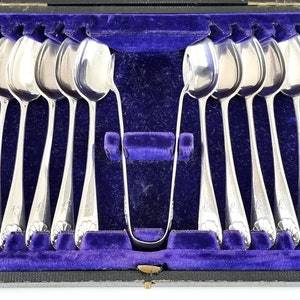 Puede incluir: Un juego de 12 cucharaditas de plata y una pinza para azúcar en una caja de madera forrada de terciopelo azul.