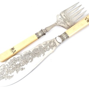 Puede incluir: Un juego de cubiertos de plata con un cuchillo y un tenedor. Ambas piezas tienen diseños florales ornamentados y mangos de marfil. Los mangos están grabados con las iniciales "W.A."