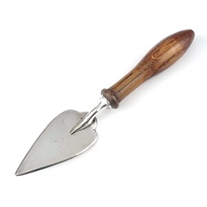 May include: A silver-colored pie server with a heart-shaped blade and a wooden handle. The handle is a light brown color with visible wood grain. The server has a classic design, suitable for serving cakes and pies.
