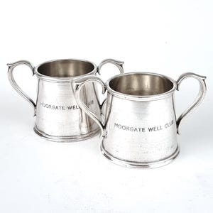 May include: Two silver cups with handles. The cups are engraved with the text "Moorgate Well Club".