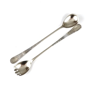 May include: A set of two silver-plated serving spoons with ornate handles. The spoons have a long, slender design and are ideal for serving desserts or salads.