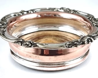 May include: A two-tone metal bowl with a silver-colored rim and decorative floral accents. The interior and lower portion of the bowl are copper-colored. The bowl has a round shape and is likely used for decorative purposes.