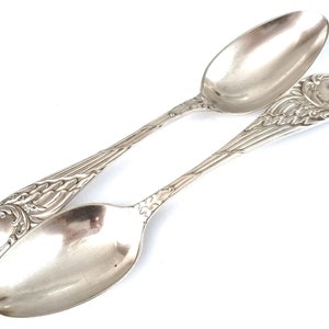 Puede incluir: Dos cucharas de plata con mangos ornamentados. Las cucharas tienen un diseño floral y un cuenco redondeado.