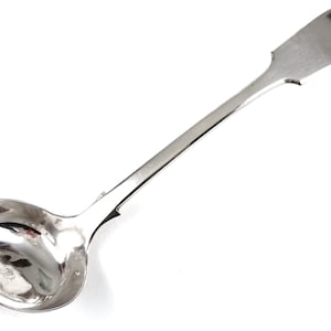 May include: A silver ladle with a long, curved handle. The handle has a decorative design and is marked with the letter "J".