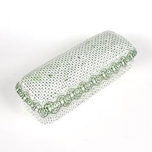 Puede incluir: Una caja rectangular de cerámica blanca con un diseño estampado en verde y blanco. La caja tiene un borde decorativo con un patrón repetitivo de hojas verdes y espirales.