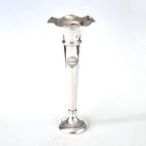 May include: A silver vase with a fluted top and a round base. The vase has a circular inscription on the side.