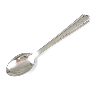 Può includere: Un cucchiaino d'argento con una ciotola rotonda semplice e un manico leggermente decorato. Il manico presenta un motivo decorativo nella parte superiore.