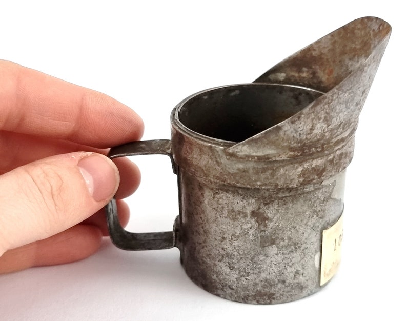Pu&ograve; includere: Una vecchia lattina di olio in metallo con un beccuccio e un manico. La lattina &egrave; arrugginita e ha un'etichetta sul lato.