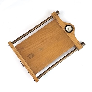May include: A wooden frame with a compass and ruler. The frame is made of light wood and has a brass finish. The compass is in the upper right corner of the frame and the ruler is on the left side.