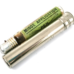 May include: A silver metal tube with a green and black label that reads "MIDGE APPLICATION "PEN". The tube contains a small glass vial with a brown liquid.