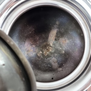 May include: Close-up of the inside of a silver-colored metal container. The interior is dark gray and has a textured surface with small, dark spots.