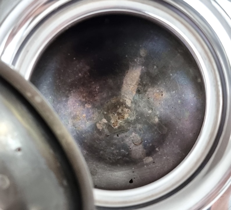 May include: Close-up of the inside of a silver-colored metal container. The interior is dark gray and has a textured surface with small, dark spots.