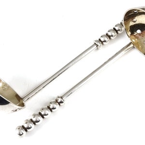 May include: Two silver tea strainers with beaded handles. One strainer has a round, perforated bowl, the other has a bowl shaped like a small ladle.