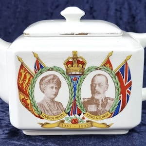 May include: White ceramic teapot with a square body and a lid. The teapot features a commemorative design with portraits of Queen Mary and King George V, surrounded by flags and a crown. The text "Queen Mary", "King George", and "1910 - 1935" is printed on the teapot.