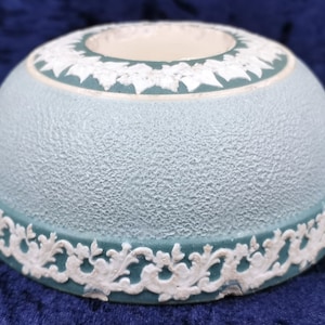 May include: A light blue ceramic bowl with a white floral design around the rim. The bowl has a textured surface and a slightly domed shape.