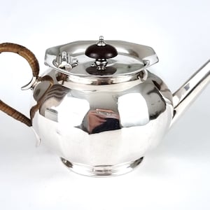 May include: A silver teapot with a wooden knob on the lid and a woven wicker handle.