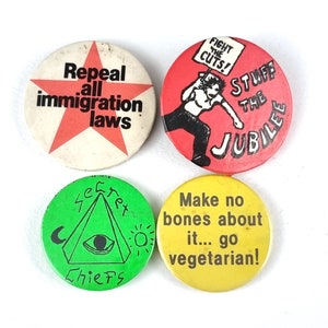 Op de afbeelding: Vier ronde button badges met verschillende berichten. De eerste badge is rood met een witte ster en de tekst "Repeal all immigration laws". De tweede badge is rood met een witte omtrek en de tekst "Fight the cuts! Stuff the Jubilee". De derde badge is groen met een witte driehoek en de tekst "Secret Chiefs". De vierde badge is geel met de tekst "Make no bones about it... go vegetarian!"