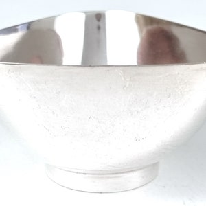 May include: A silver bowl with a smooth, reflective surface. The bowl has a rounded shape and a slightly flared rim.