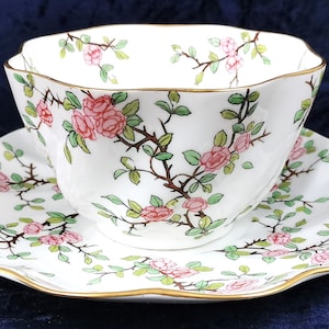 Könnte beinhalten: Ein weißes Tee-Set mit einem zarten Blumenmuster aus rosa Rosen und grünen Blättern. Das Set hat einen goldenen Rand.