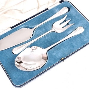 May include: A set of three silver serving pieces in a blue velvet lined box. The set includes a serving spoon, a serving fork, and a cake server.