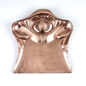 May include: A copper dustpan with an ornate Art Nouveau design. The dustpan has a curved handle and a wide, shallow body.