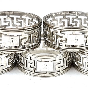 Peut inclure: Ensemble de cinq anneaux de serviette en argent avec un motif de clé grecque et les chiffres de 1 à 5 gravés sur chaque anneau.