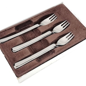 May include: Three silver forks in a brown velvet box. The forks are arranged in a row, with the prongs facing up.