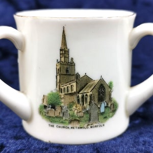 Puede incluir: Taza de cerámica blanca con dos asas, con una ilustración en blanco y negro de una iglesia con un alto campanario y el texto "THE CHURCH, METHWOLD, NORFOLK".