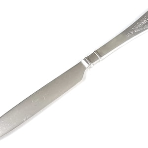 May include: A silver butter knife with a crown and floral design on the handle. The knife is about 8 inches long.