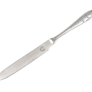Puede incluir: Un cuchillo de mantequilla de plata con un mango decorativo y una hoja dentada.