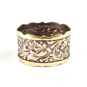 May include: A gold and copper ring with an intricate floral design. The ring is wide and has a scalloped edge.