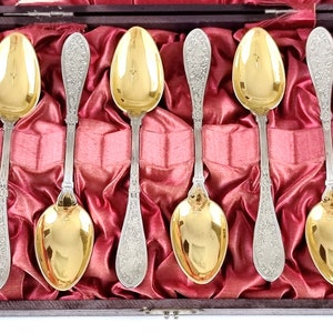Pode incluir: Conjunto de seis colheres de prata com colheres douradas, apresentadas em uma caixa de madeira forrada de veludo vermelho.