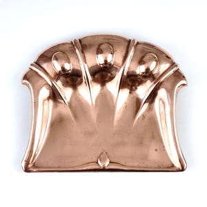 May include: A copper dustpan with a fan-shaped design and three decorative knobs. The dustpan is made of polished copper and has a smooth, shiny surface.