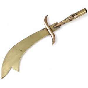 Puede incluir: Un abridor de cartas de latón con forma de cimitarra con un mango de latón y cobre. El mango es un casquillo de bala reutilizado con un diseño de corona.