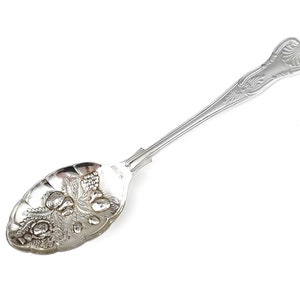 May include: A silver serving spoon with an ornate handle and a bowl decorated with an embossed design of fruit and leaves.