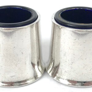 Puede incluir: Dos saleros de plata con forros de vidrio azul. Los saleros son redondos y tienen una base acampanada.