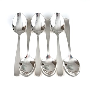 May include: A set of five polished silver spoons with oval bowls and long, slender handles. The spoons are arranged in a row, reflecting the bright light. The spoons are a part of a dining set.