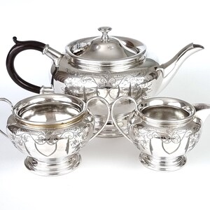 May include: A silver tea set with a teapot, creamer, and sugar bowl. The set has an ornate design with floral motifs and a heart shape in the center.