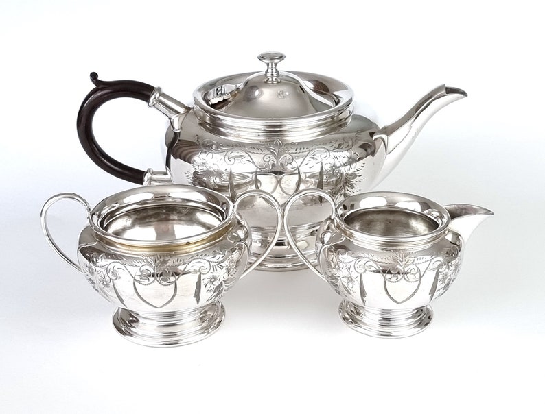 May include: A silver tea set with a teapot, creamer, and sugar bowl. The set has an ornate design with floral motifs and a heart shape in the center.