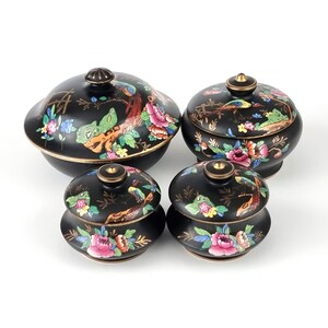May include: Four black ceramic decorative lidded bowls with floral and bird designs. The bowls have gold trim and are in various sizes. The lids feature colorful flowers and birds.
