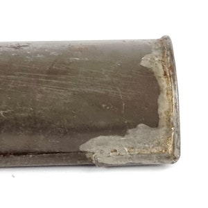 Pu&ograve; includere: Primo piano dell'estremit&agrave; di un tubo metallico marrone con parte della vernice scheggiata, che rivela il metallo sottostante.