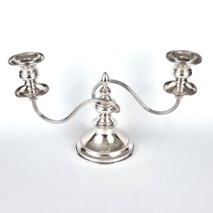Peut inclure: Un candélabre en argent avec deux bras et une base centrale. Les bras sont incurvés et chacun possède un bougeoir. La base est décorée d'un motif en relief.