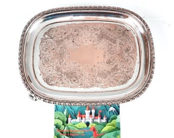 Puede incluir: Una bandeja rectangular de plata para servir con intrincados patrones florales y de volutas grabados. La bandeja tiene un borde con cuentas y una superficie pulida. Es una pieza vintage, adecuada para servir alimentos o como objeto decorativo.