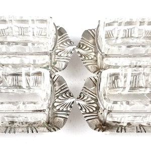 Puede incluir: Juego de cuatro saleros plateados con insertos de vidrio transparente. Los saleros tienen un diseño decorativo y ornamentado.